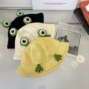 Détail des bobs grenouille en noir, beige et jaune avec yeux 3D et broderie décorative