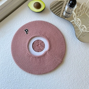 Detail of pink knitted beret featuring a black letter P patch on soft wool texture