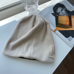 Detail of beige ribbed knit beanie with letter L patch on a cozy lifestyle background