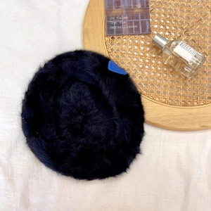 Detail of black faux rabbit fur beret with a small blue heart patch on soft fabric