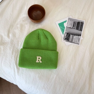 Detail van een felgroene gebreide muts met een witte letter R-patch op de omslag
