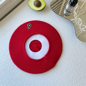 Close-up of red knit beret with P letter patch and textured ribbed knit details