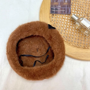Detail of warm brown plush beret with black bow accent and adjustable inner drawstring