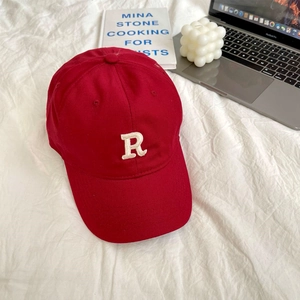 Close-up of red cotton baseball cap with white embroidered R letter on white fabric