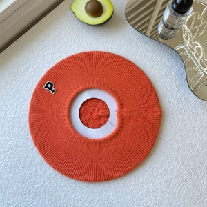 Detail of orange knitted beret featuring a classic letter P embroidery on the side