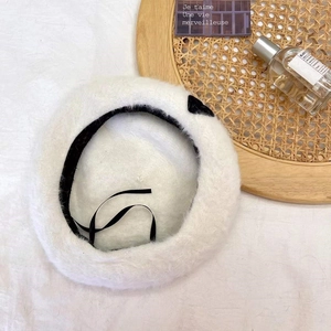 Detail of white plush beret featuring black velvet bow and silk ribbon straps