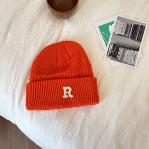Close-up van oranje gebreide muts met R-letter patch op witte stoffen achtergrond