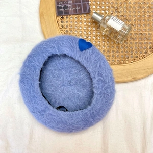Detail of lavender plush beret with blue heart embroidery on woven tray