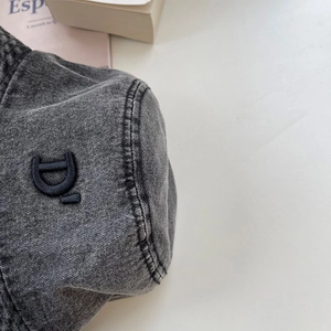 Dettaglio del logo ricamato nero sulla texture del cappello alla pescatora in denim grigio