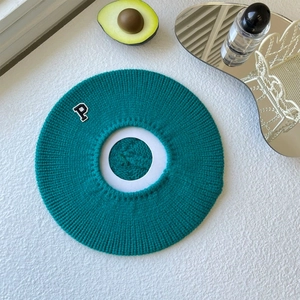 Close-up of knit beret in peacock green featuring embroidered P letter patch on knit fabric