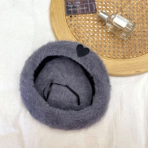 Close-up of soft grey-purple faux fur beret with black heart patch and adjustable drawstrings