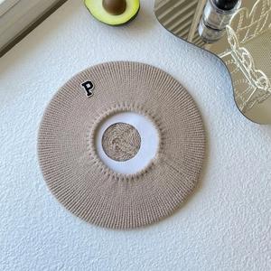 Close-up of knit beret in khaki with a decorative letter P patch on textured surface