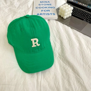 Close-up of a green baseball cap with white letter R embroidery on a clean desk