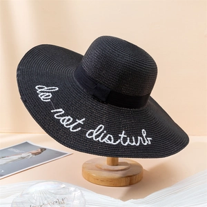 Detail of black wide-brim straw hat featuring 'do not disturb' embroidery and ribbon