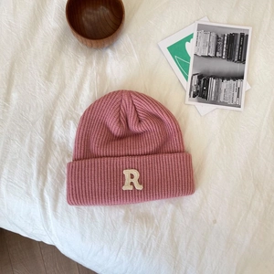 Detail van de roze gebreide muts met R-patch op een gestructureerde stoffen ondergrond