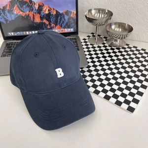 Detail van donkerblauwe baseballpet met wit geborduurde letter B op modern bureau