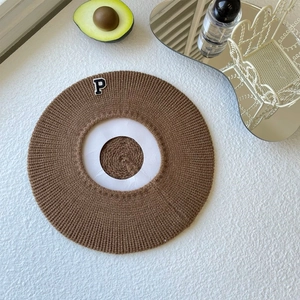 Close-up of a brown knitted beret with a stylish embroidered P patch on a white desk