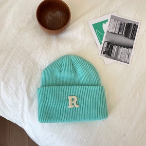 Detail van mintgroene gebreide muts met witte letter R patch op gestructureerde stof