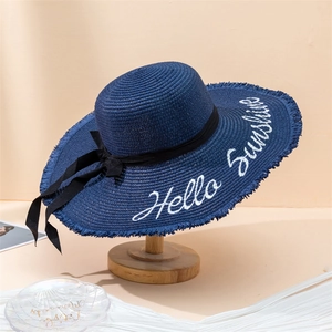 Detail of dark blue straw hat with Hello Sunshine embroidery and black bow decoration