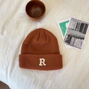 Detailopname van roestbruine gebreide muts met witte letter R patch op zachte witte stof