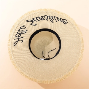 Detail of Hello Sunshine embroidery on a beige wide brim straw hat with fringe edge