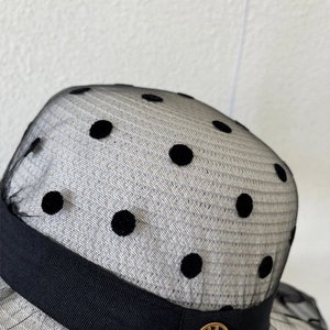 Détail d'un chapeau de soleil en tulle à pois noir avec ruban satin et logo doré