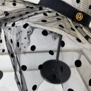 Détail du tulle à pois et logo métallique doré sur un chapeau de paille à large bord