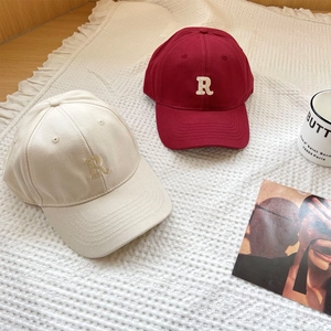 Detail of cream and burgundy cotton baseball caps with embroidered R logo on textured cloth