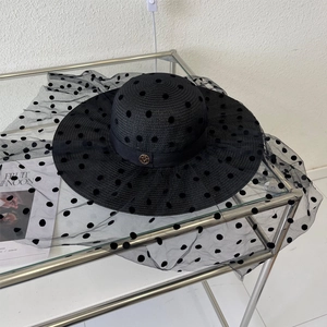 Détail d'un chapeau de paille noir avec voile en résille à pois et emblème M doré
