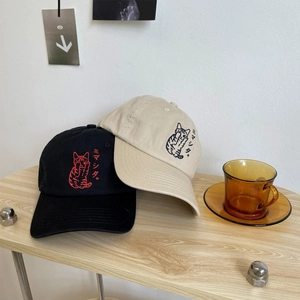 Black and beige cotton baseball caps with cat embroidery on a wooden table surface