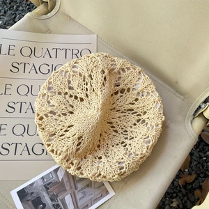 Détail d'un béret en crochet beige ajouré avec des motifs tissés sur une chaise en toile