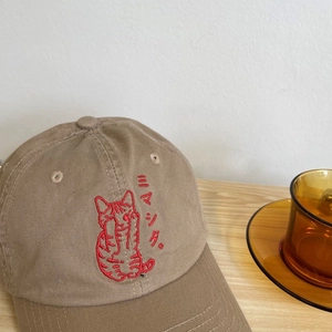 Close-up of cat embroidery and Japanese text on a khaki cotton baseball cap
