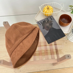 Detail van caramel suede vissershoed op houten standaard met herfstdecoratie en tijdschrift