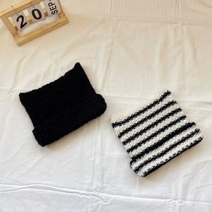 Close-up of thick knitted cat ear beanies in black and striped patterns on white fabric