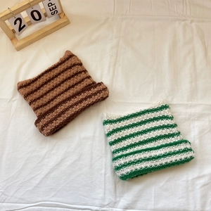 Flat lay of cat-ear knit beanies in coffee and green stripes on white fabric
