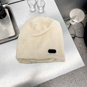 Dettaglio del berretto in maglia a nido d'ape beige con etichetta rettangolare nera