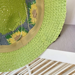 Detail van handgeweven groene strohoed met heldergele zonnebloemborduring op de stof