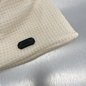 Dettaglio macro del berretto beige in maglia a nido d'ape con etichetta fatta a mano