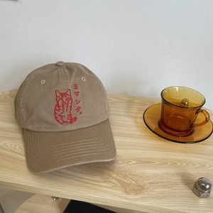 Detail of khaki cotton baseball cap with red cat embroidery on wooden background