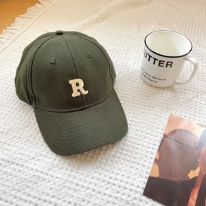 Detailed top view of a dark green cotton baseball cap with R letter embroidery on a rug