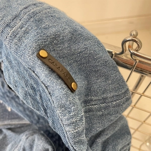 Detail of the light blue denim beret featuring a brown leather tag with metal rivets