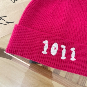 Dettaglio del berretto in maglia rosa acceso con ricamo 1011 e trama a coste morbida
