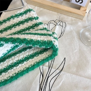 Detail of green and white striped knit hat with thick wool texture in a cozy home setting