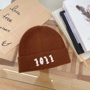 Dettaglio del berretto in maglia marrone con ricamo numerico 1011 bianco e trama morbida