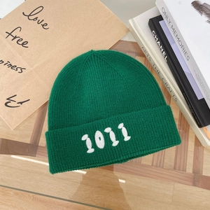 Dettaglio del berretto in maglia verde scuro con ricamo numerico 1011 bianco