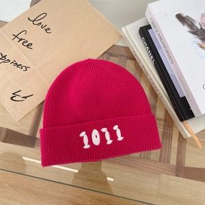 Dettaglio berretto in maglia rosa acceso con ricamo bianco dei numeri 1011 sul risvolto