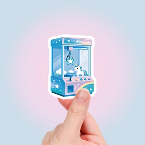 Close-up of a hand holding a cute unicorn claw machine sticker with pastel rainbow colors