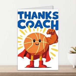 Close-up of a basketball coach thank you card with superhero cartoon design on a wooden desk