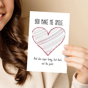 Close-up of a hand holding a Valentine card with a red heart and You Make Me Smile text
