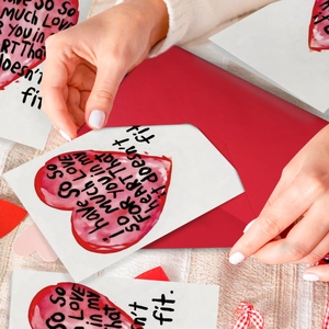 Mani che tengono un biglietto d'auguri con cuore ad acquerello e busta rossa su lino
